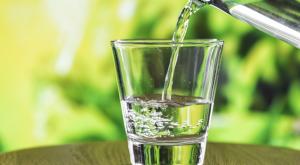 Glass with water being poured into it on a table with greenery in background